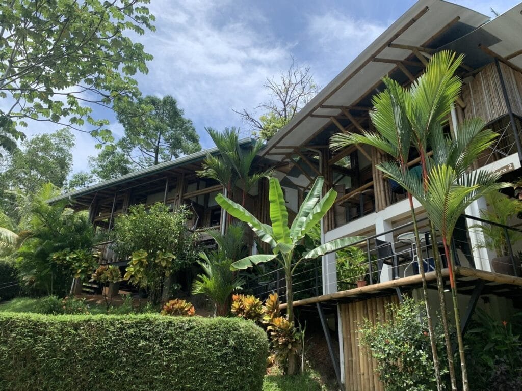 Edificio moderno rodeado de vegetación tropical, con balcones y diseño arquitectónico integrado a la naturaleza. Ideal para ecoturismo y escapadas en un entorno natural.
