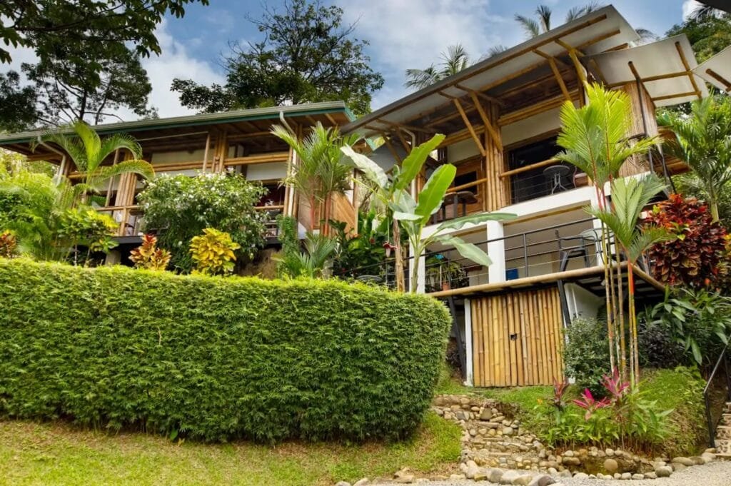 A charming wooden house surrounded by lush greenery and vibrant flowers, featuring a well-maintained garden and a pathway leading to the entrance. The structure showcases a blend of natural materials and modern design elements.