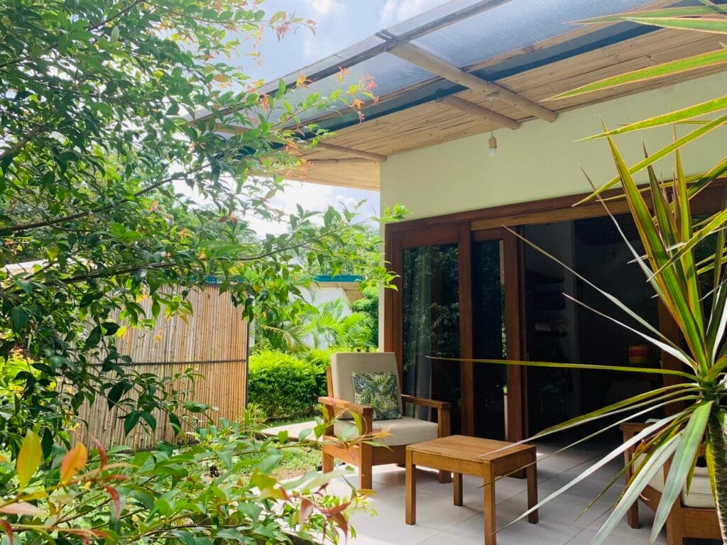 Terraza acogedora con muebles de madera, rodeada de vegetación exuberante y un ambiente tranquilo. Ideal para relajarse al aire libre en un entorno natural.