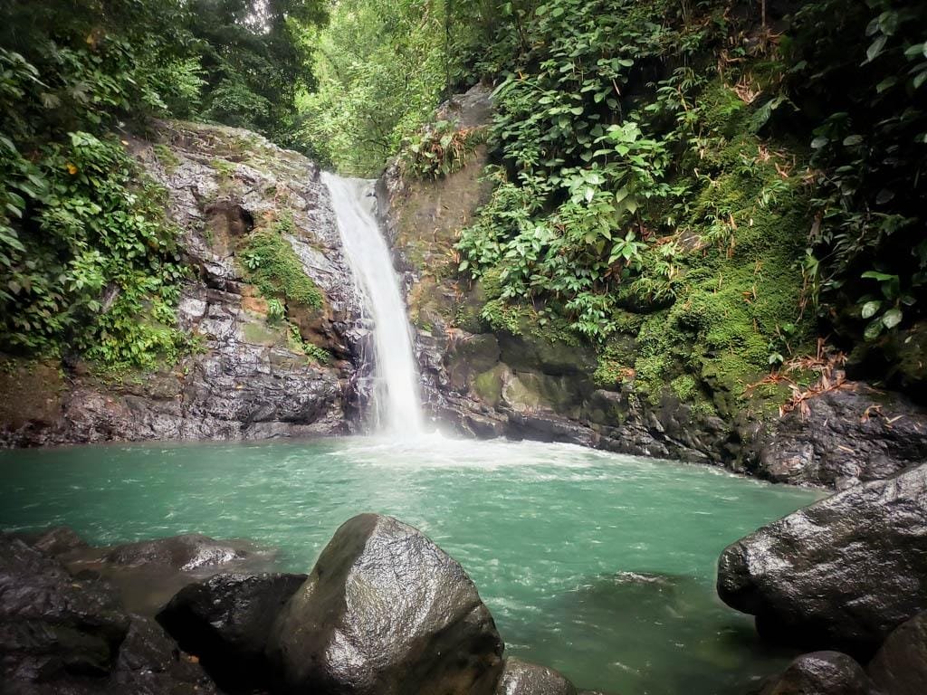 Serene waterfall cascading into a turquoise pool surrounded by lush greenery and large rocks, showcasing the beauty of nature.