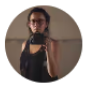 Autorretrato de una mujer con gafas, sosteniendo una cámara en un entorno minimalista. La imagen muestra su enfoque en la fotografía y la creatividad.